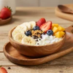 Açaí bowls 4 Eine Schale Açaí-Bowl mit Banane, Beeren, Granola und Kokosraspeln auf einem hellen Tisch